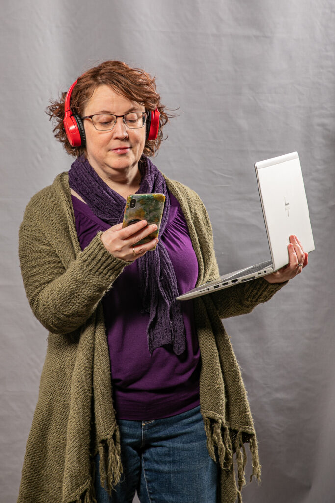 Woman wearing red headphone holding laptop and smartphone